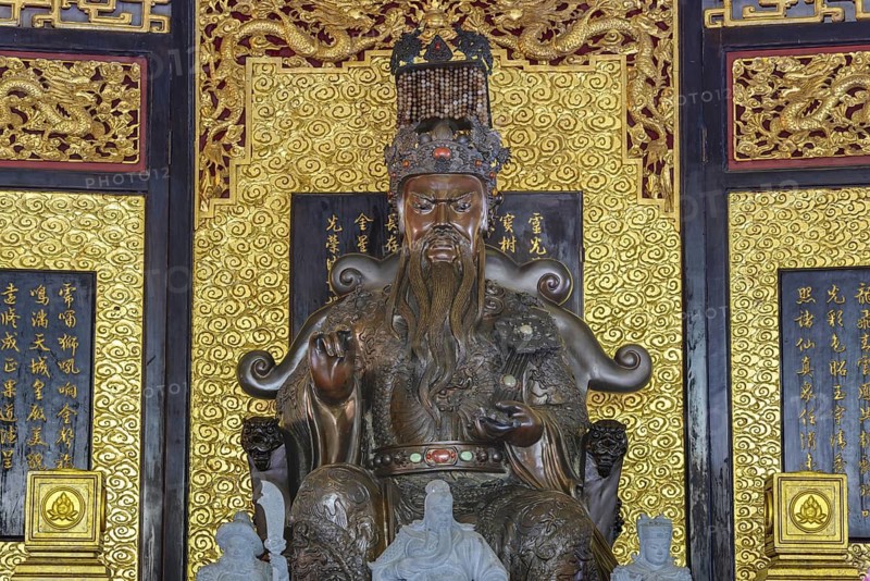 A deity seated majestically on a throne, Shou Xing (also known as Shou Lao or Nanji Xianweng), the god of longevity, carved from dark wood with gold inlays, surrounded by dragon motifs and cloud patterns, symbolises wisdom and long life in Chinese-Daoist culture, Chee Chin Khor Temple, Bangkok, Thailand