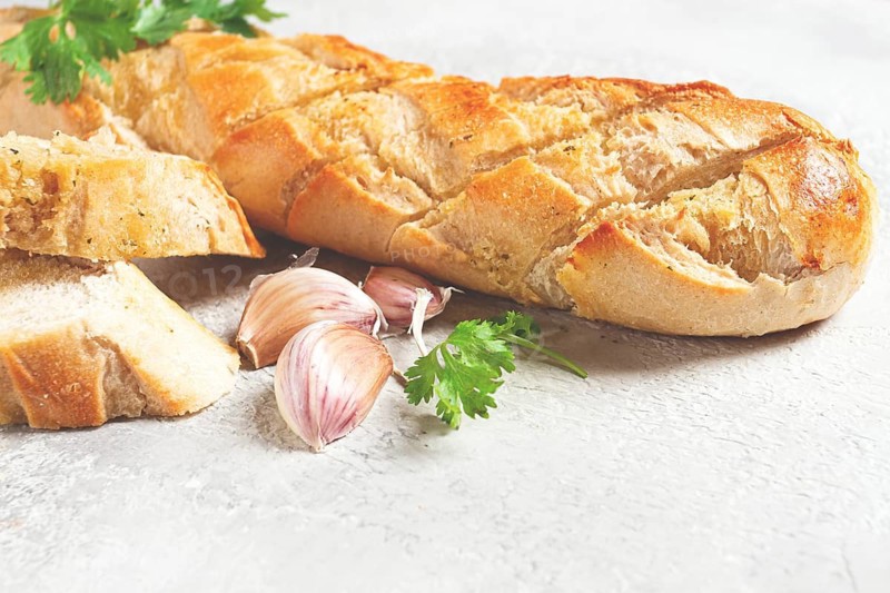 Garlic bread, baguette with garlic butter and herbs, on a light table, top view