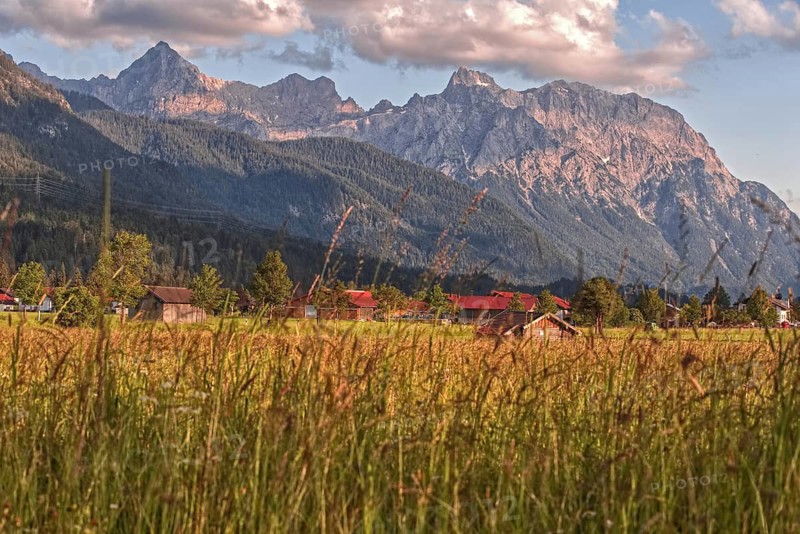 Idyllic village at the foot of the mountains with rich fields and clouds in the sky in an alpine setting, Wallgau, Bavaria, Germany