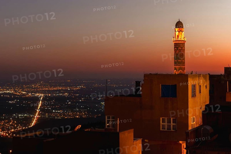 Illuminated mosque minaret above Mardin old town with glowing city lights and Mesopotamian plains at sunset. Great Mosque of Mardin Ulu Camii Minaret