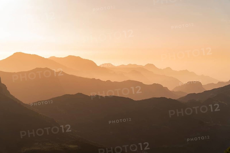 Golden sunset casting a soft glow over the layered mountain ranges seen from the viewpoint near Roque Nublo in Gran Canaria