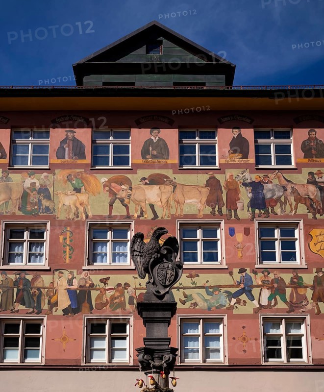 Eagle fountain, fountain column with sculpture of an eagle with city coat of arms from 1738 on the Eagle Fountain, behind it façade painting on town house, old town, Wangen im Allgäu, Bavaria, Germany
