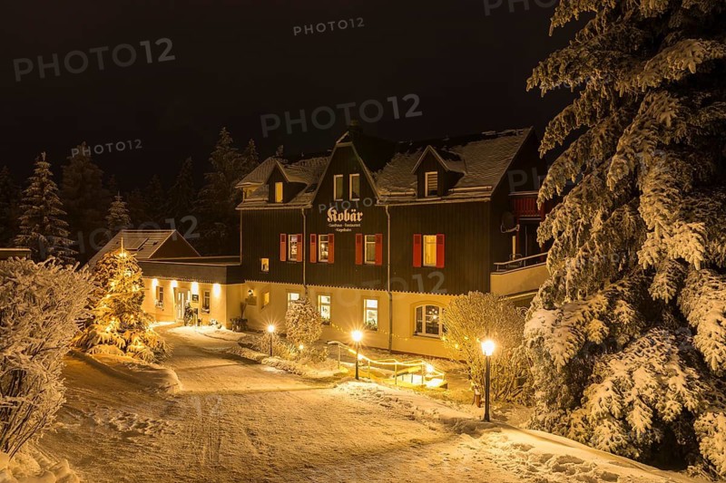 Snow-covered Gasthaus Kobär with Christmas tree at night, winter in Oberbärenburg, Altenberg, Saxony, Germany