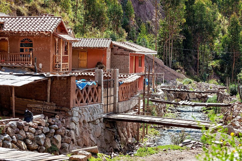 Rustic clay houses near a wooden bridge over a small river in rural surroundings, village with traditional houses in the Andes of Peru