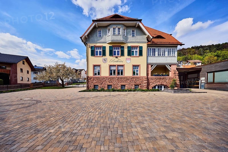 Town hall, commercial building, façade with windows, shutters and façade painting, hipped roof, paving walkway, hill, coniferous forest, blooming tree, blue sky, cumulus clouds, cirrus clouds, Am Mühlbach, Waldaschaff, Lower Franconia, Aschaffenburg district, Bavaria, Germany