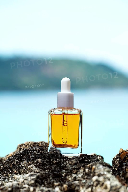 A cosmetic serum bottle with vitamins showcased on rocky seaside terrain, complemented by a tranquil ocean backdrop