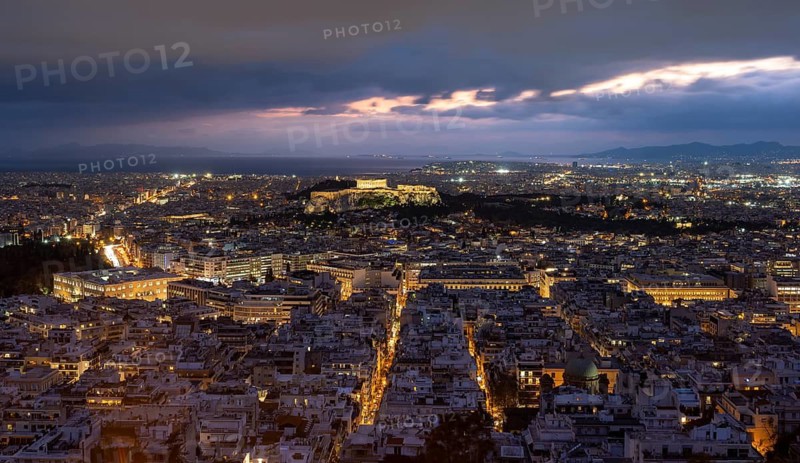 View over the sea of houses of Athens, illuminated Parthenon temple on the Acropolis, dramatic cloudy sky at sunset, from Mount Lycabettus, Athens, Greece