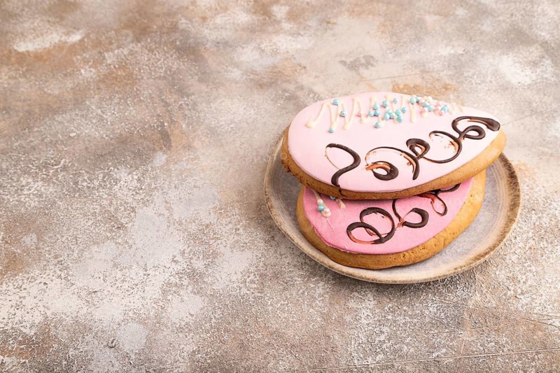 Glazed pink and blue decorated cookies, on brown concrete background, copy space, side view