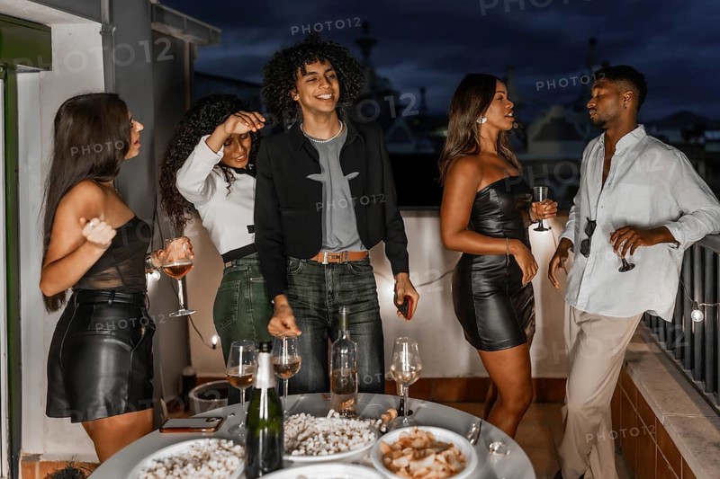 Happy elegant and multi-ethnic young friends celebrating a night party in a roof