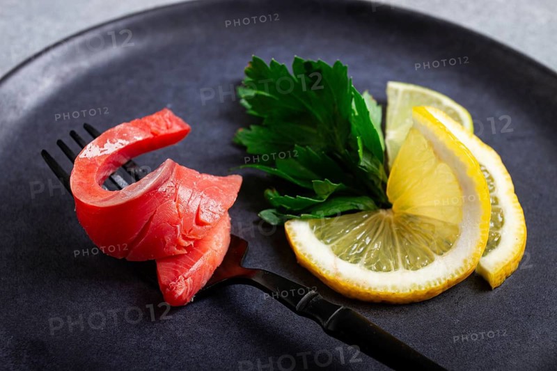 Chum salmon, cold smoked, on a fork, with lemon and parsley, top view, close-up, no people