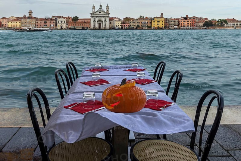 Halloween pumpkin on a set restaurant table on the shore in windy weather, Guidecca, back Venice, Veneto, Italy