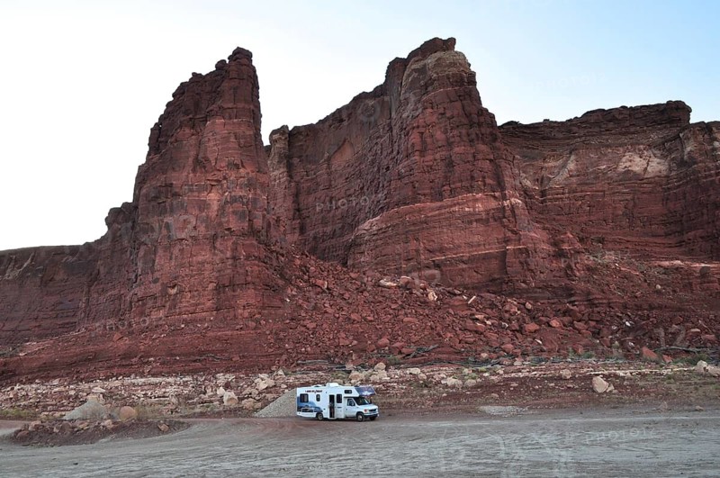An RV stands in front of massive red rocks in a tranquil desert atmosphere, Lake Powell, Arizona, USA
