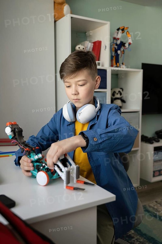 A young boy with headphones intently builds a robot at home, showcasing creativity and concentration. The clean and organized room highlights a focus on learning and technology
