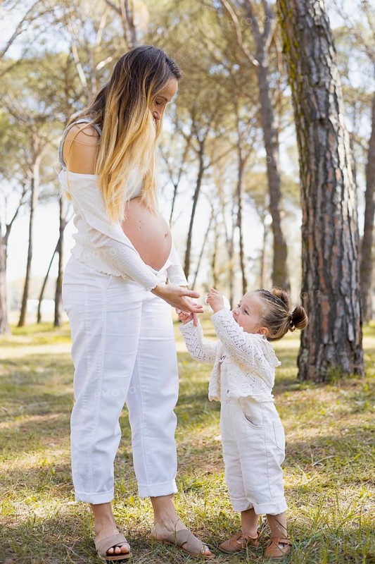 A serene moment between a pregnant woman and her daughter in a lush forest. The child joyfully interacts with her mom, creating a warm and tender family scene