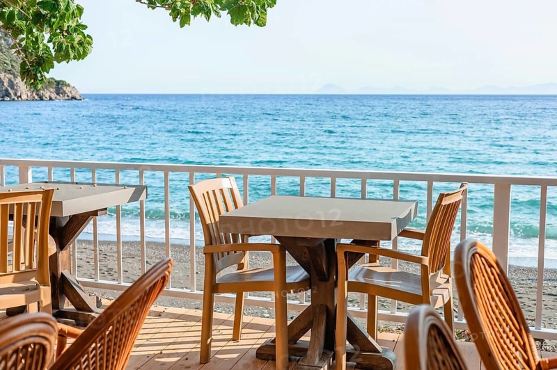 Brightly lit seaside dining space features wooden tables and chairs with stunning ocean views, perfect for relaxation