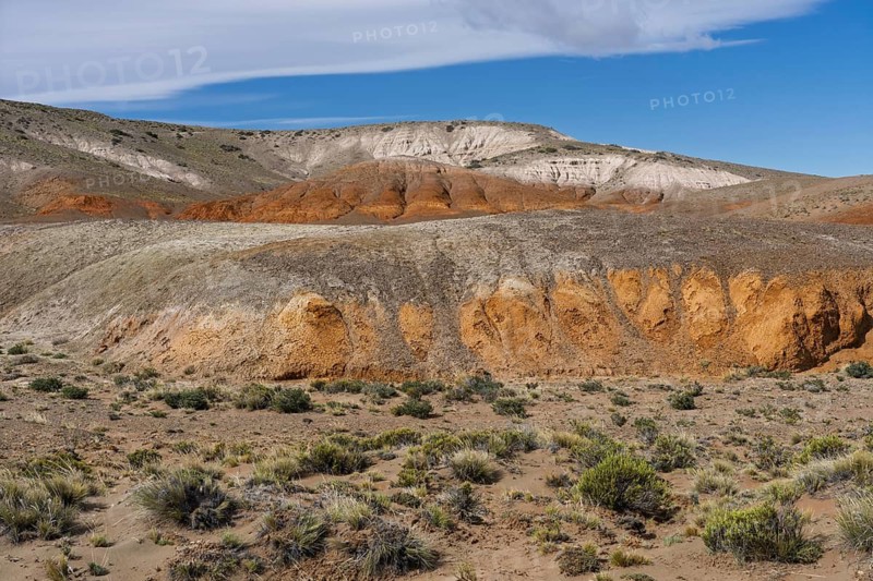 Colored sediment layers in arid hills, badlands with red-orange and white erosion formations, steppe vegetation in the foreground, Santa Cruz province, Patagonia, Argentina