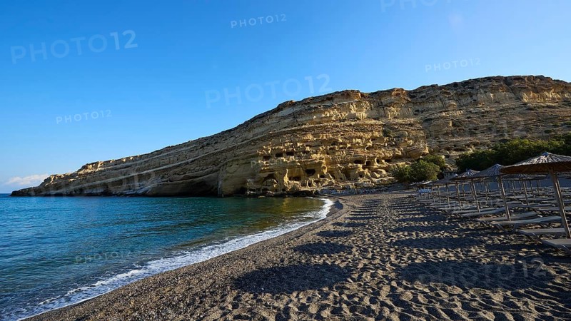 Neolithic caves, former hippie paradise, sandy beach with umbrellas and impressive rocks in front of calm sea, Matala, south coast, Crete, Greek Islands, Greece