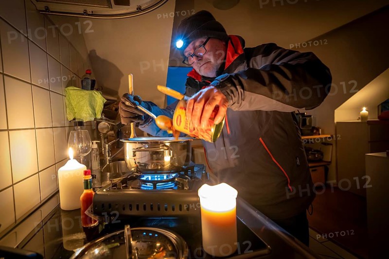 Symbolic picture blackout, extensive, prolonged power failure, in private settings, without electricity, heating, water, cooking in the kitchen, heating food with a gas-powered camping stove, which is also approved for indoor use