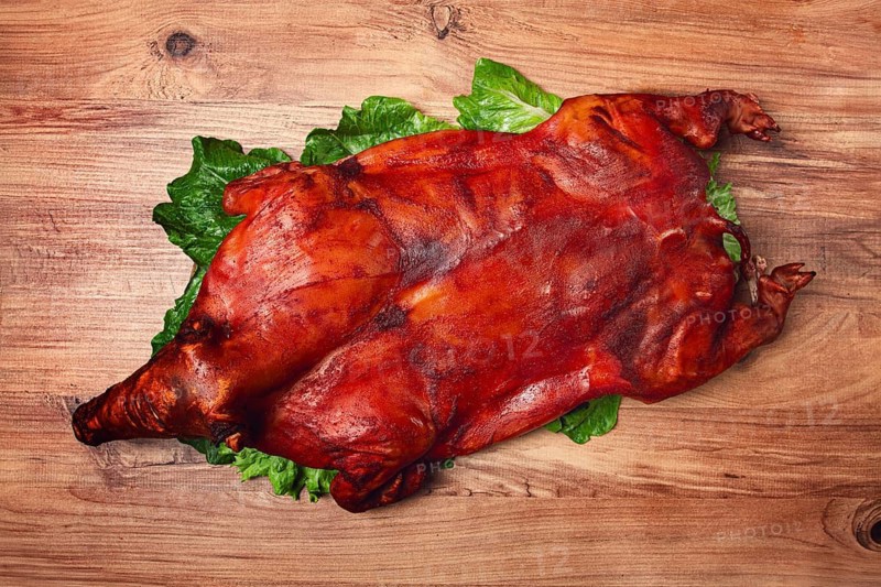 Baked, fried piglet, on a wooden table, no people, The whole piglet is baked and served on the leaves of a fresh green salad, showing off its crispy skin and detailed features