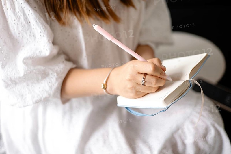 A person writes in a notebook, wearing a white dress and bracelet, creating a calm and focused atmosphere