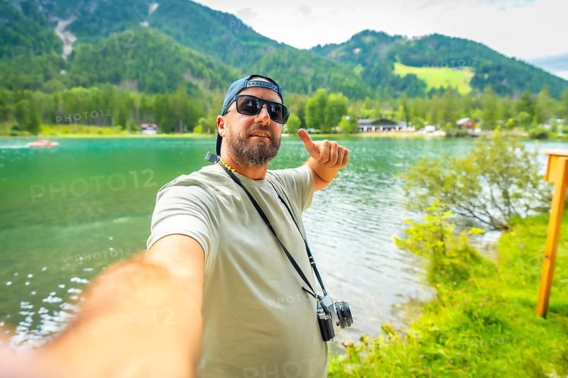 Tourist enjoying summer holidays at lake dobbiaco in the italian dolomites, taking a selfie and gesturing thumbs up