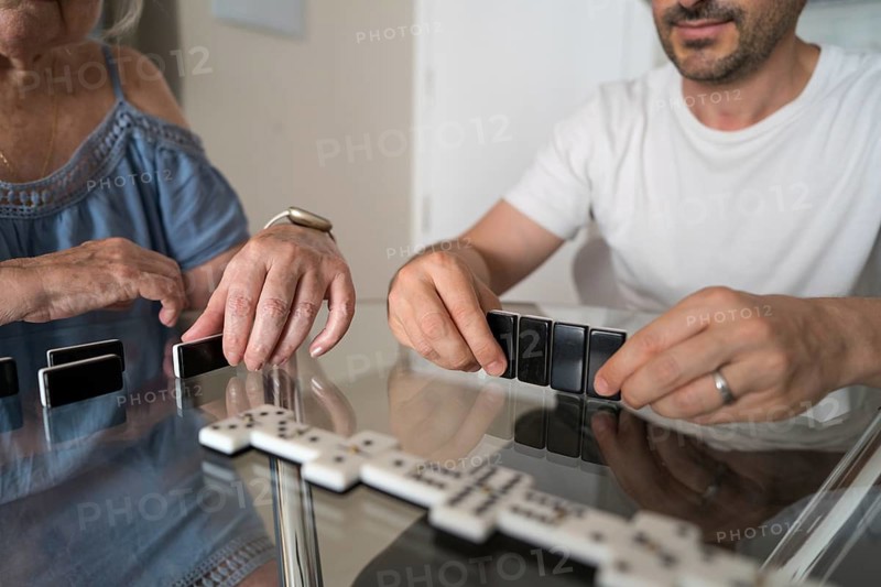 A cheerful multigenerational family sits together in the kitchen engaged in a lively game of dominoes, sharing laughter and quality time as they enjoy each other's company