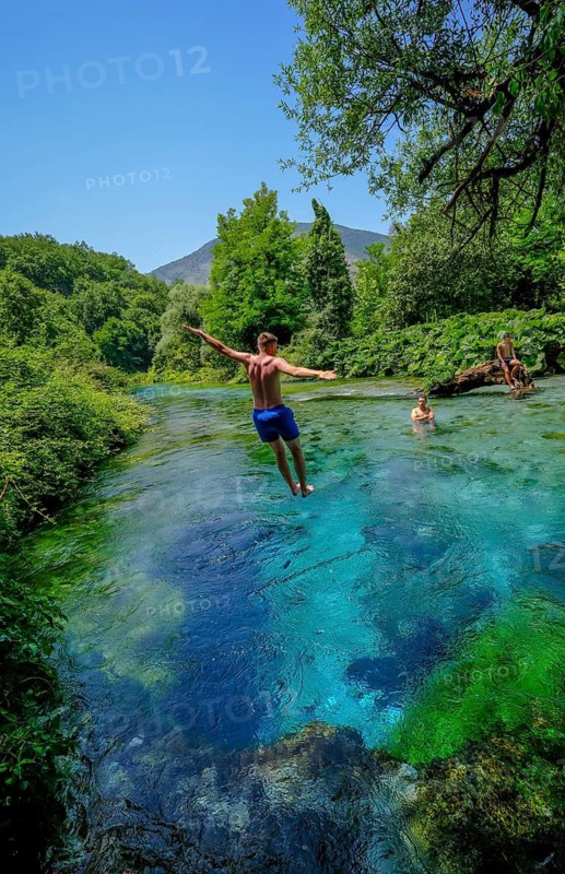 Muzina, Albania, tourists bathe in the Syri i Kaltër, THE BLUE EYE, is the country's most water-rich spring at 6 metres per second. The water emerges from a spring pot at a depth of more than 50 metres under high pressure. The water temperature is a fairly constant 12.75°C. The Blue Eye is located midway between the larger towns of Saranda on the coast and Gjirokastra inland