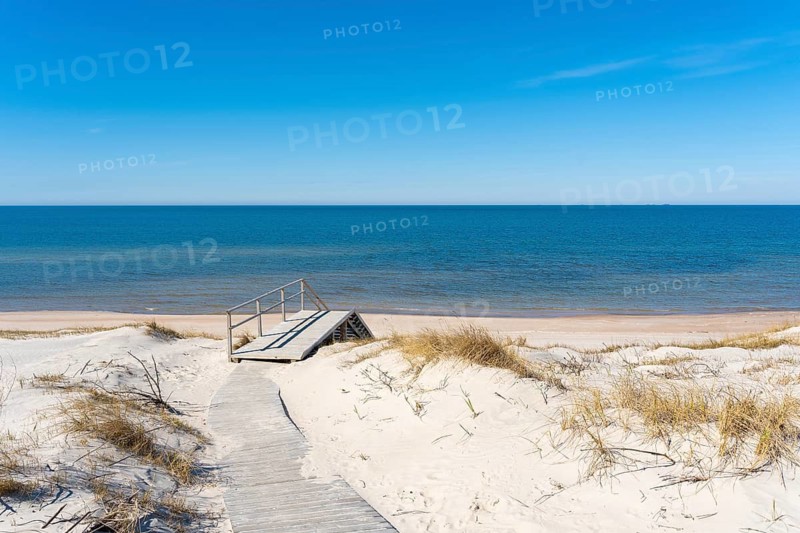 A wooden walking path leading to the stairs to the beach on the Curonian Spit on the Baltic Sea, Lithuania, A tranquil beach scene with sand dunes, a wooden boardwalk, and a calm ocean under a clear blue sky, Curonian Spit, Neringa, Lithuania