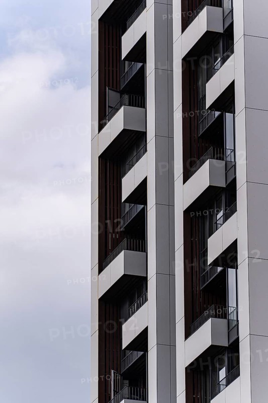 Close-up of a contemporary high-rise building showcasing sleek design elements and geometric patterns against a backdrop of a cloudy blue sky. Modern urban architecture in focus