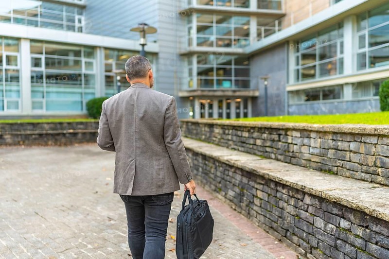 Rear view of a mature businessman with laptop bag walking in the city to work
