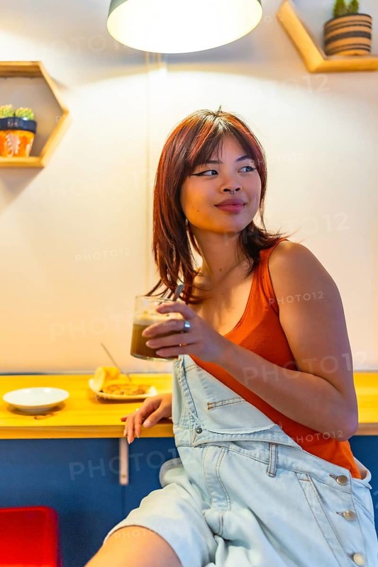 Vertical portrait of an asian beauty young distracted woman enjoying coffee in a modern cafeteria