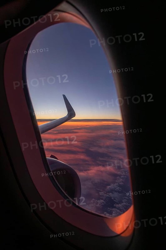 A captivating view from an airplane window showing a vibrant sunset with pink and purple clouds. The sleek wing is visible against the colorful sky, evoking a sense of wanderlust