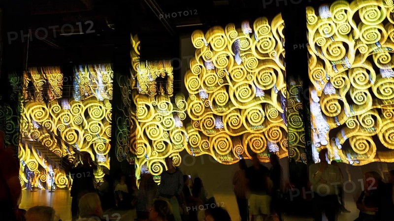 Visitors look at swirling patterns, spirals, gold, yellow, immersive exhibition, digital art, colorful projections on walls, Gustav Klimt, motion blur, art museum, Port des Lumieres, Westfield Überseequartier, Hafencity, Hamburg, Germany