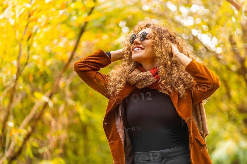 Woman wearing sunglasses and casual clothes looking up in a park during autumn