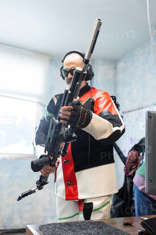 A blind athlete prepares for an Olympic shooting event. The image showcases the athlete's focus and determination, equipped with headphones and a specialized rifle