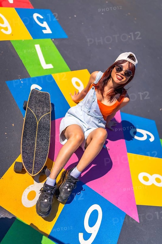 Vertical top view of a chinese young woman with skate sitting above a colorful graffiti in a park
