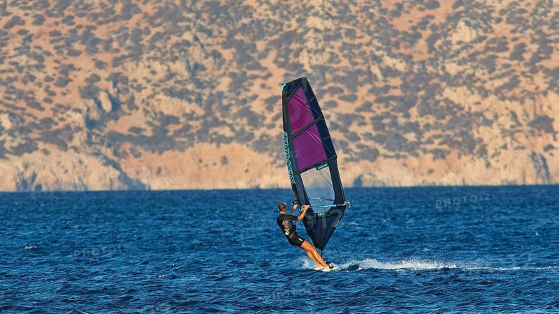 A windsurfer sails fast over the blue water in front of a mountain backdrop, windsurfer, Meltemi windsurfing spot, Devils Bay, Paralia Vatha, Vatha Beach, south-east coast, Karpathos, Dodecanese, Greek Islands, Greece