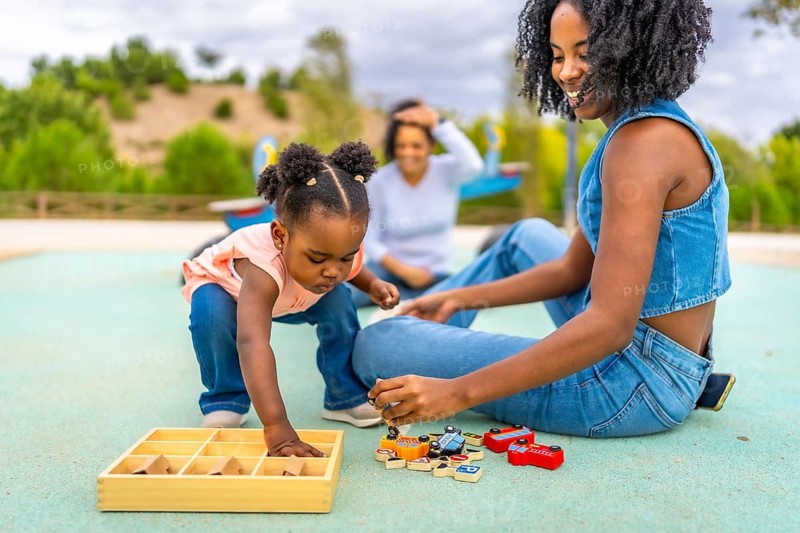 Little african girl messing with toys from a box playing with family in an outdoor park