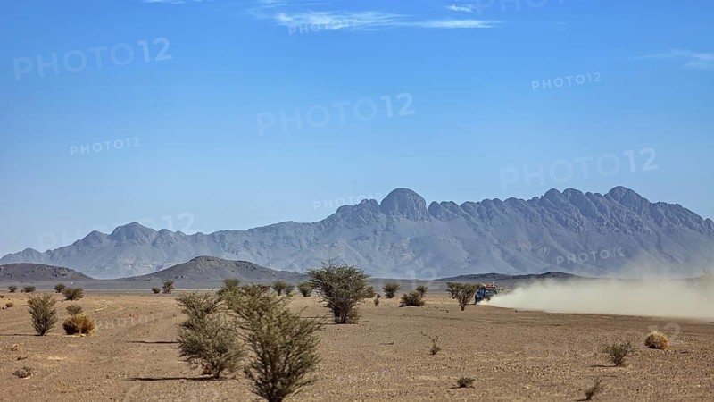 Off-road vehicle in a dusty desert landscape with mountains and trees, Off-road vehicle through the endless landscape of the Sahara desert in Algeria