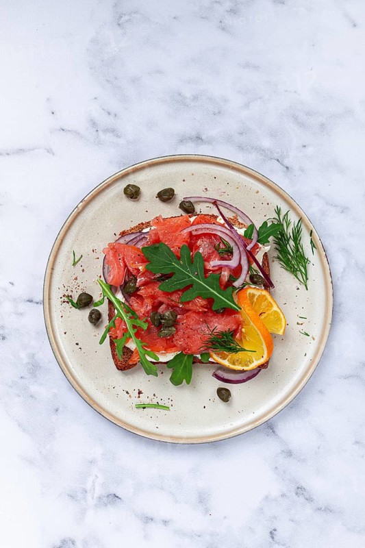 Sandwich with freshly smoked salmon, on black bread, with cottage cheese, with herbs and red onions, capers and pieces of citrus fruits, on a marble countertop, breakfast, no people