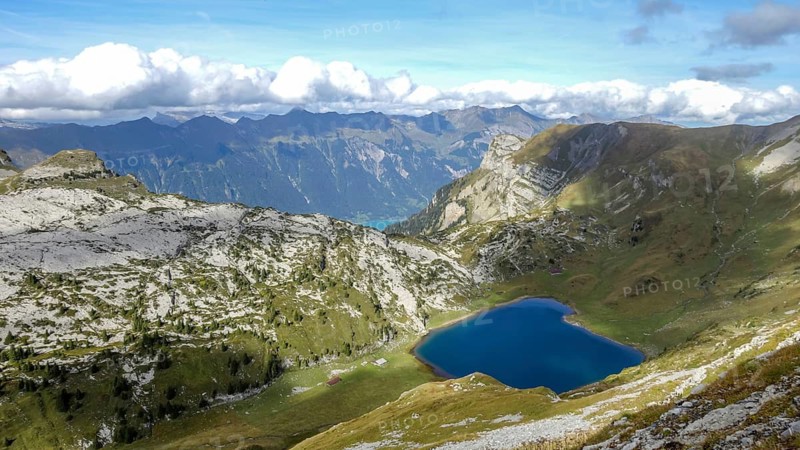 Scenic summer view of a tranquil mountain lake nested in the verdant Alpine ranges, under a clear blue sky with fluffy clouds