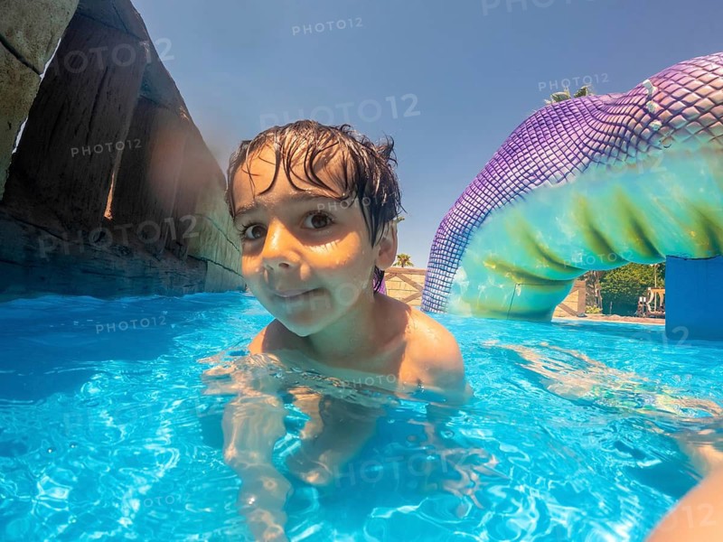 Young boy swimming in blue pool at water park, enjoying summer vacation on mediterranean sea in alicante