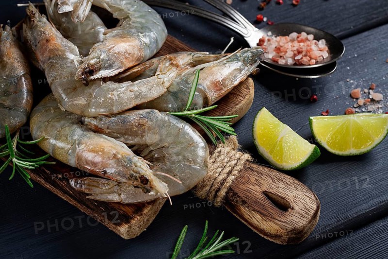 Fresh raw, white-footed shrimp, tiger prawns vannamei, on a wooden cutting board, with lime slices, and seasonings