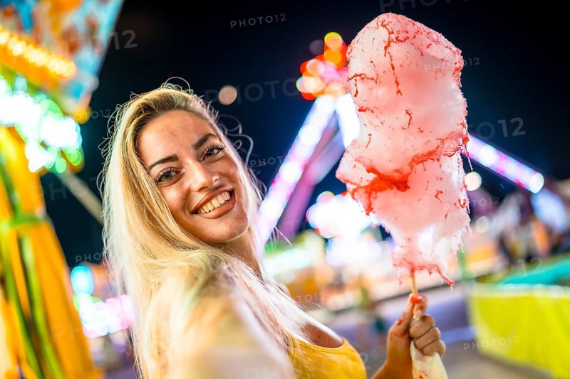 Blonde woman taking selfie holding pink cotton candy at night in an amusement park