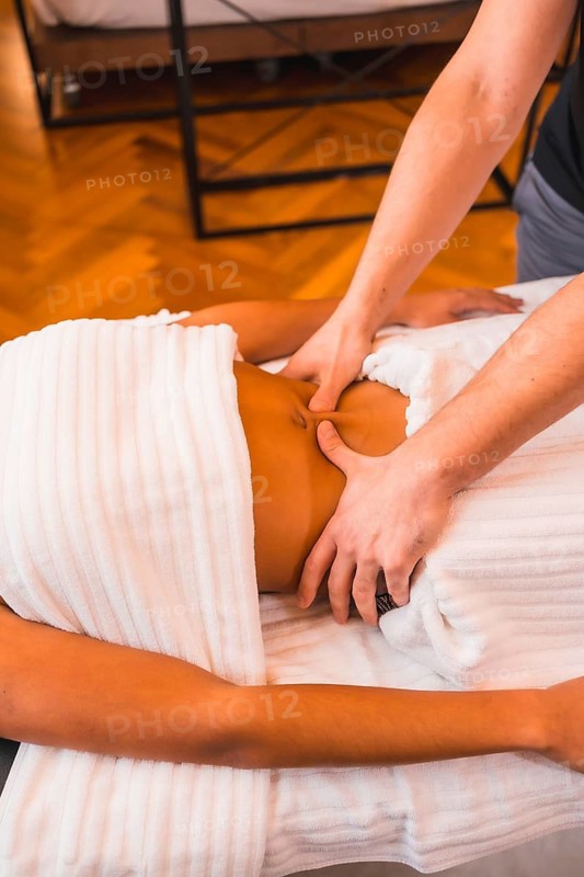 Home massage, a young man performing a massage at the client's home in the abdomen. With a face mask in the coronavirus pandemic