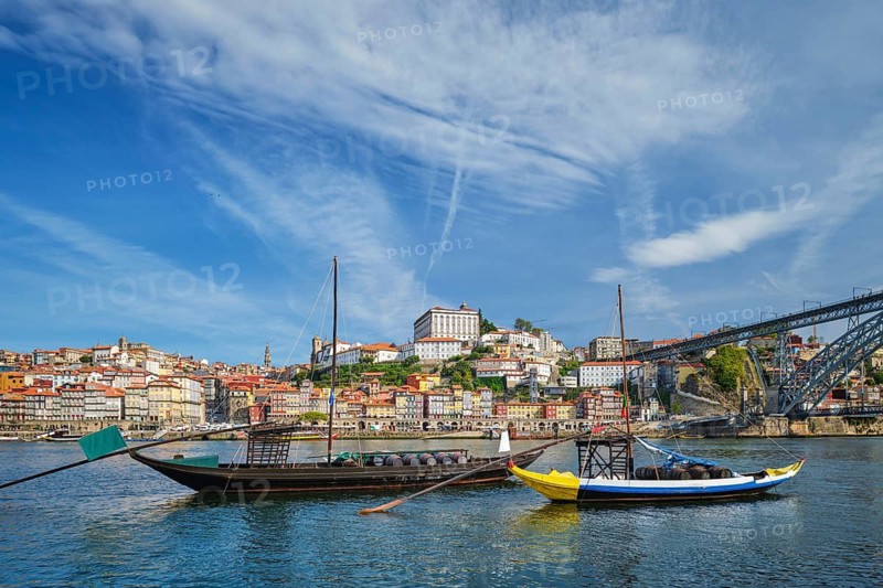 View of Porto rabelo boats on Douro River by Ribeira, Portugal, with moored traditional boats, wine barrels and Vila Nova de Gaia waterfront near Dom Luis I Bridge