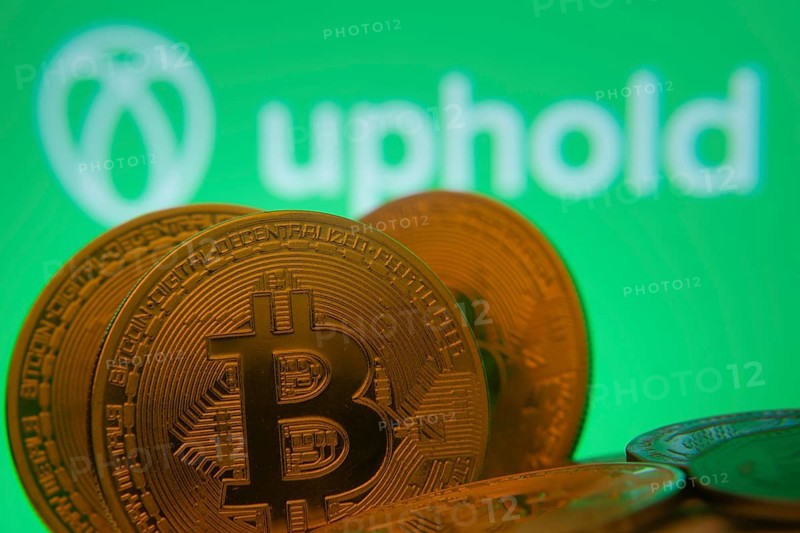Dhaka, Bangladesh- 19 Sep 2025: Close-up of Bitcoin coins with the Uphold logo visible on a screen in the background