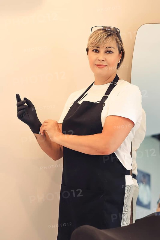 Woman wearing an apron and gloves, standing in front of a mirror, looking confident