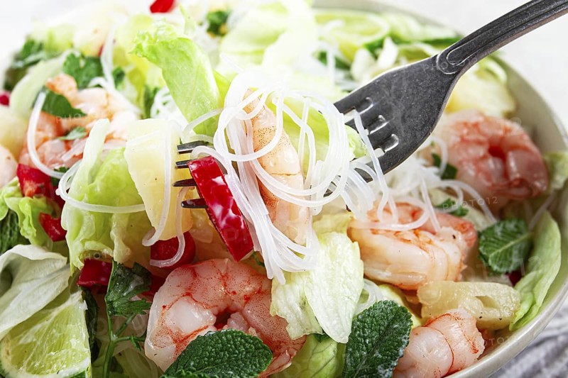 Thai salad with shrimp and rice noodles, pineapple slices, coriander and mint leaves, on a white plate, homemade, no people