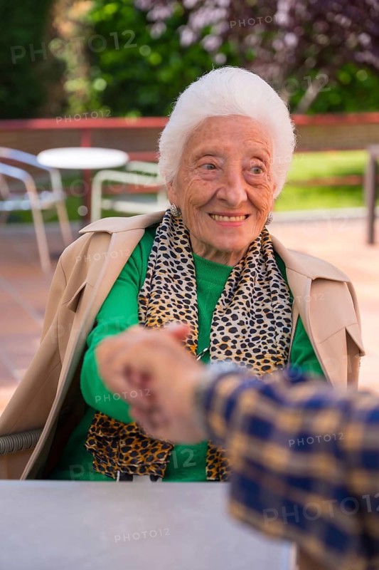 Hands of two elderly people in the garden of a nursing home or retirement holding hands in a moment of affection